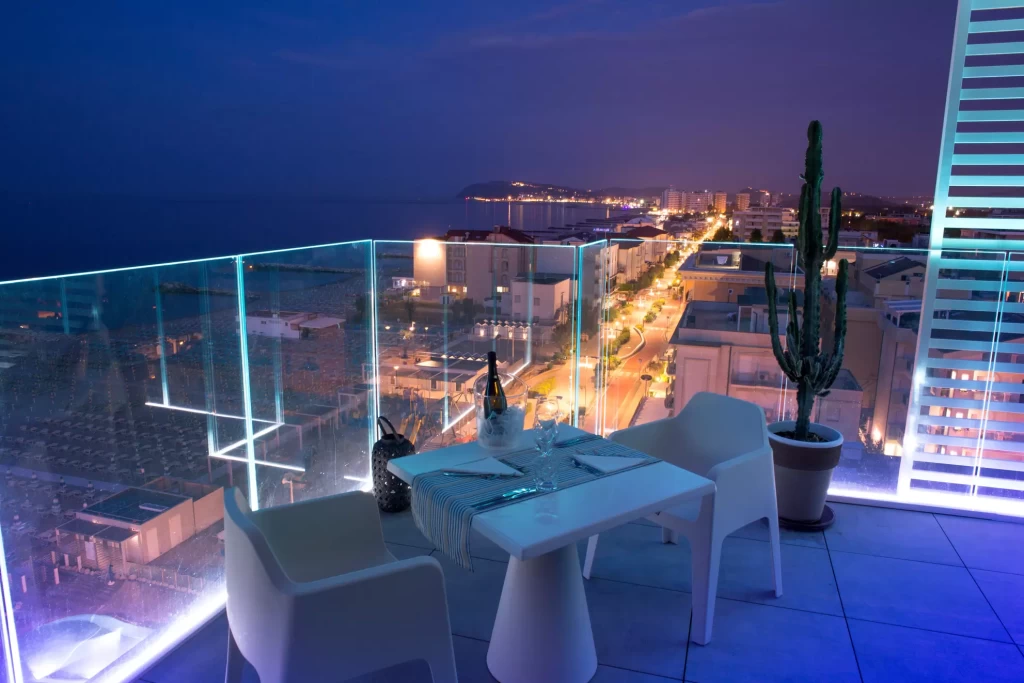 Terrazza elegante con tavolo apparecchiato e vista notturna sulla città illuminata.