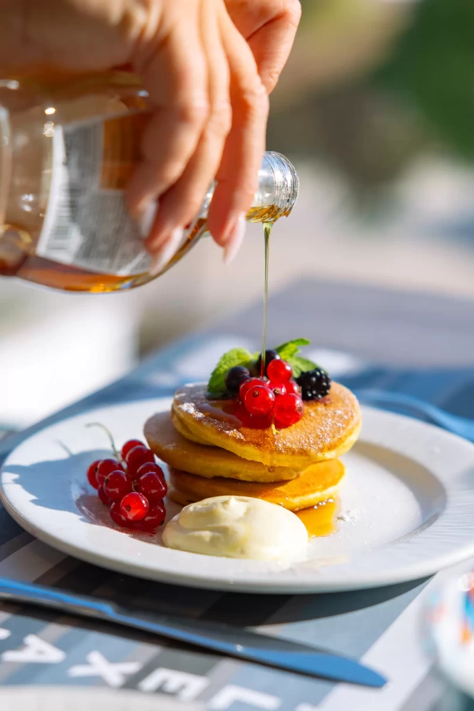 Pancake con frutti di bosco guarniti con sciroppo d'acero e crema su un piatto.