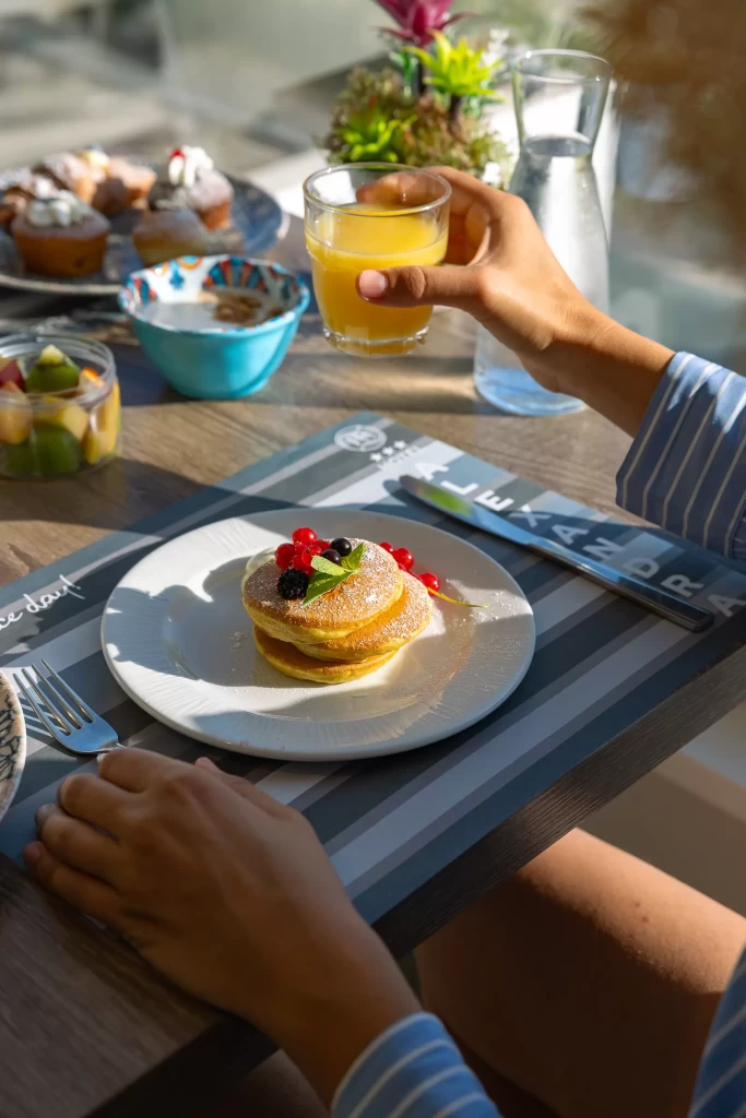 Colazione con pancake, frutta fresca e succo d'arancia su un tavolo apparecchiato.