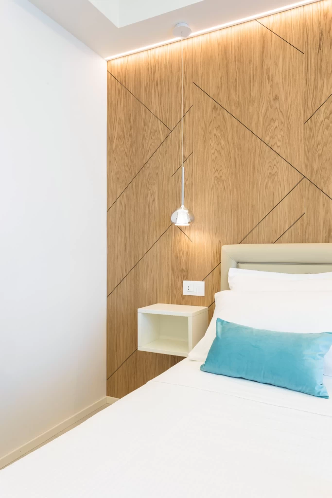 Camera da letto moderna con parete in legno, letto bianco e cuscino azzurro.