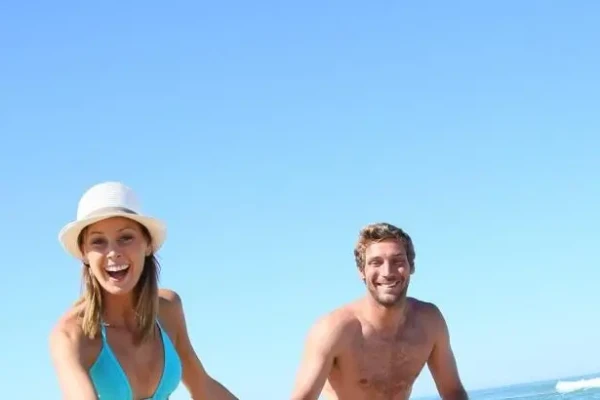 Coppia sorridente che corre sulla spiaggia in un giorno di sole.