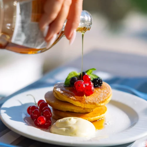 Pancake con frutti di bosco guarniti con sciroppo d'acero e crema su un piatto.