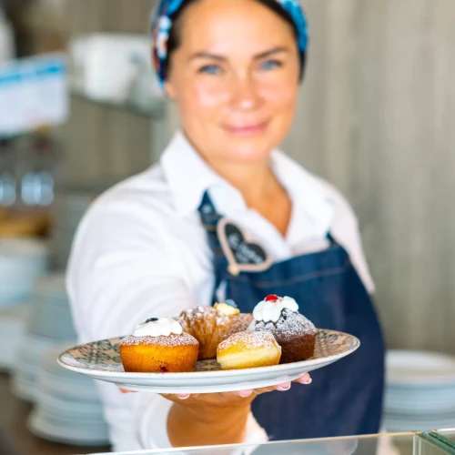 Donna con grembiule che offre un piatto di pasticcini assortiti.