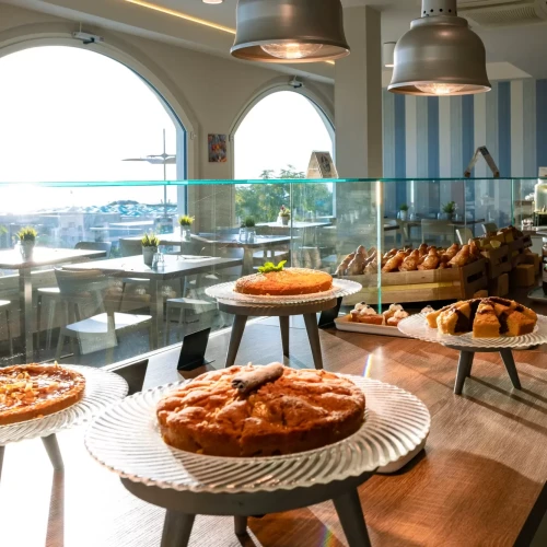 Vetrina di un bar con dolci assortiti esposti e vista sul mare attraverso ampie finestre.