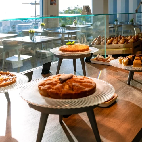 Vetrina di dolci vari in una pasticceria luminosa con tavoli sullo sfondo.