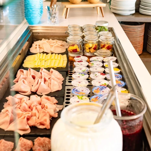 Buffet con salumi, formaggi, yogurt, marmellate e conserve di frutta in vasetti di vetro.