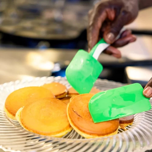 Mani che servono pancake su un piatto con una spatola verde.