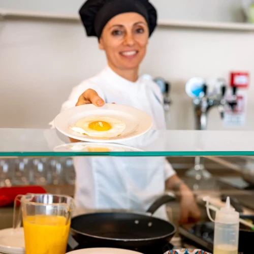 Cuoca sorridente porge un piatto con un uovo fritto in cucina.
