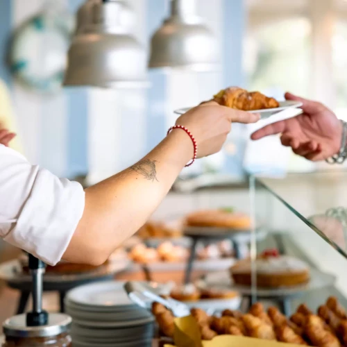 Una persona porge un piatto con un cornetto a un cliente in una pasticceria.