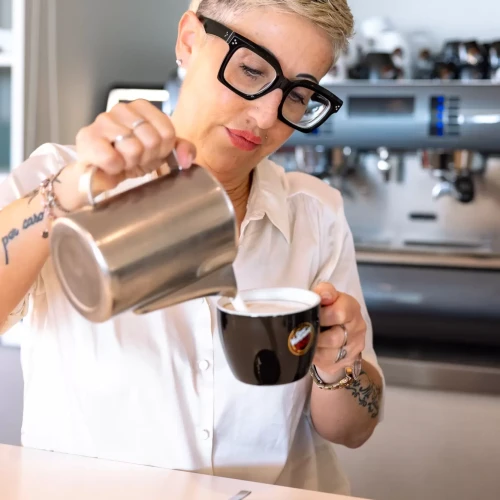 Una persona prepara il caffè versando latte in una tazza nera.