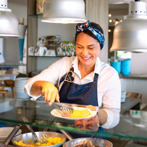 Cuoca sorridente in un ristorante serve piatti caldi da una cucina a vista.