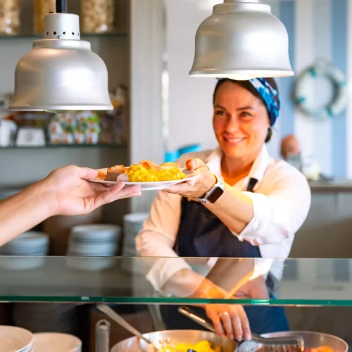 Persona che serve cibo in un ristorante, sorridente mentre consegna un piatto.