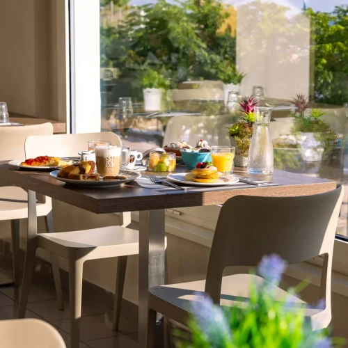 Colazione servita su un tavolo vicino a una grande finestra con vista sul giardino.