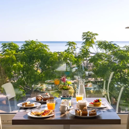 Colazione con vista mare dalla finestra di un ristorante, circondata da alberi verdi.