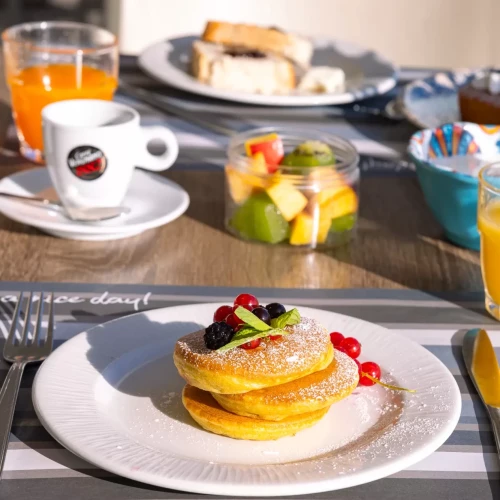 Colazione con pancake guarniti di frutti di bosco, succo d'arancia, macedonia e caffè.