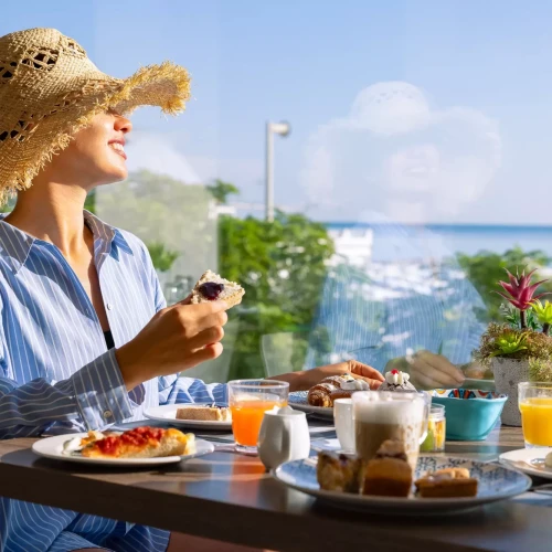 Donna sorridente che fa colazione in un ristorante con vista sul mare.