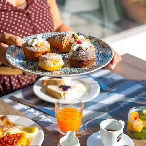 Colazione con dolci assortiti, succo d'arancia e bevande calde su un tavolo.
